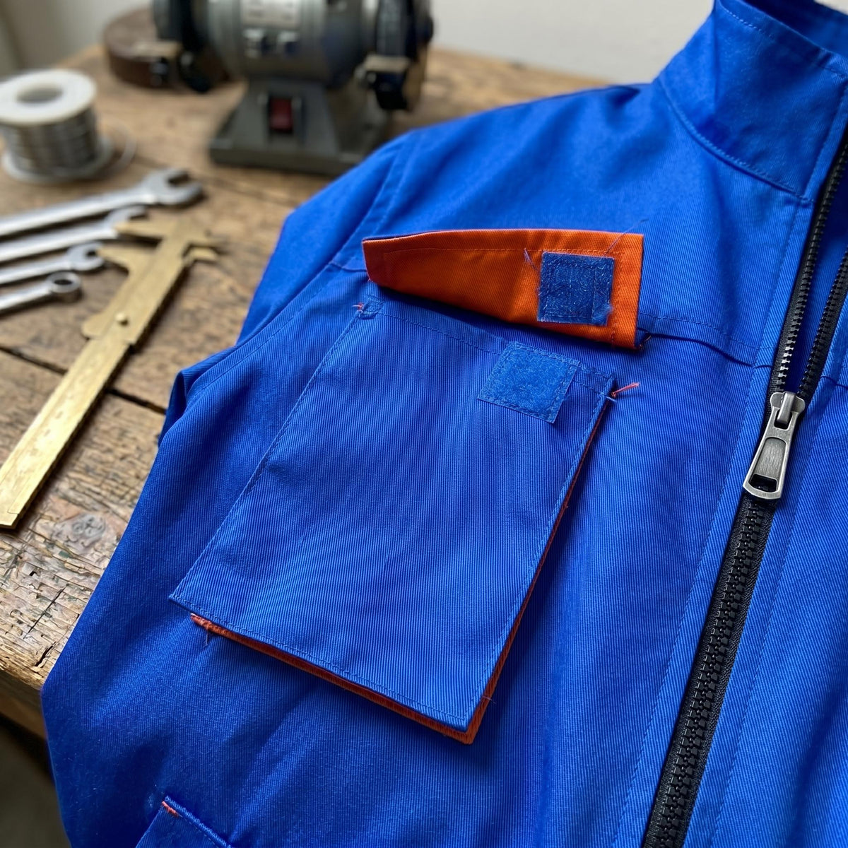 Blue work coverall chest detail with orange-lined pocket and zipper