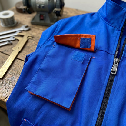 Blue work coverall chest detail with orange-lined pocket and zipper